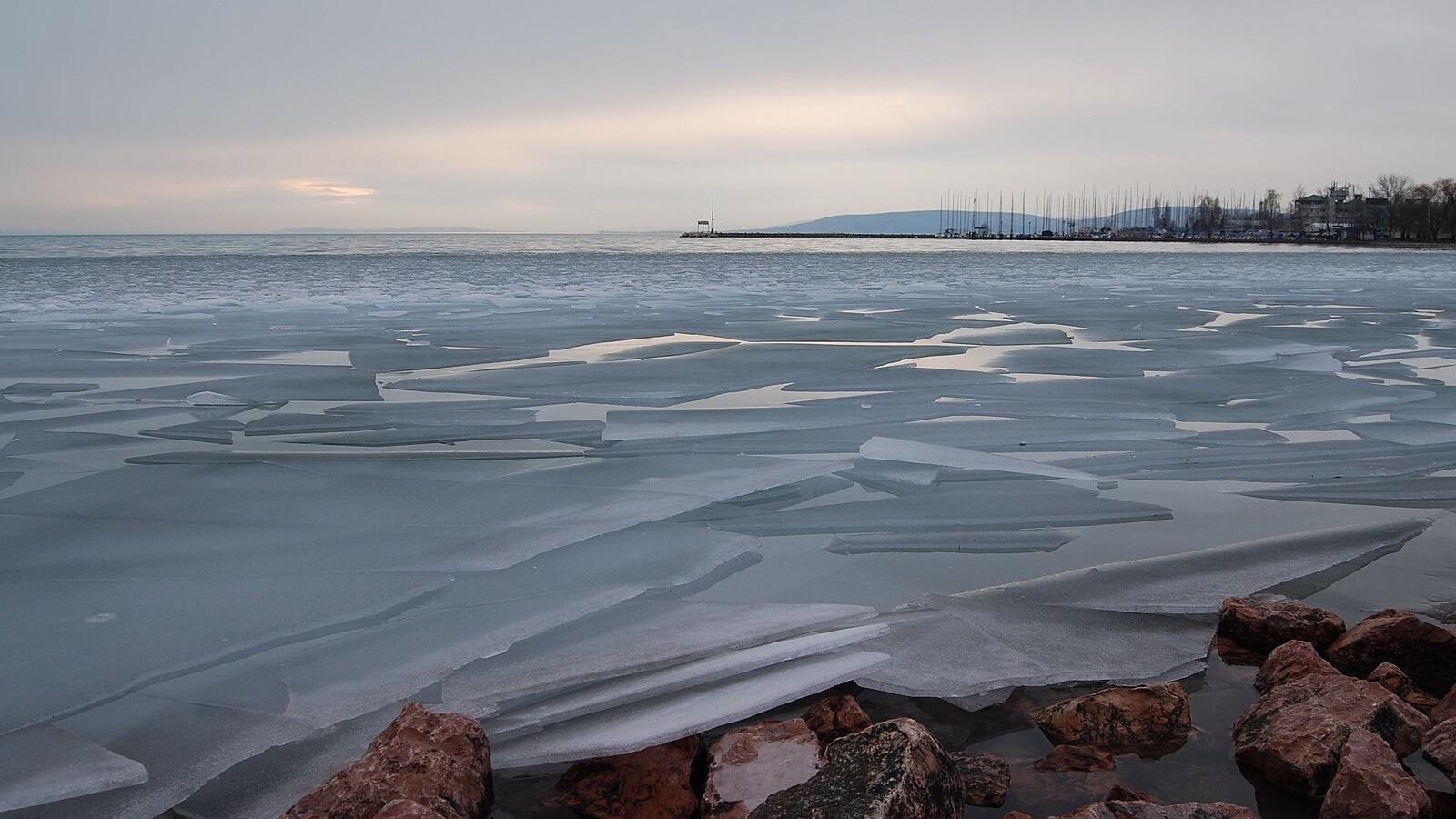 Vékony jégtáblák a téli Balaton vizén, előtérben köves part